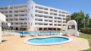Ein Hotel mit Schwimmbad, Liegestühlen und einem großen Gebäude mit mehreren Balkonen.