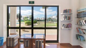 Ein Zimmer mit einem großen Fenster, einem 'SAIDA EXIT'-Schild, einem Tisch mit Stühlen und einem Bücherregal mit Büchern.