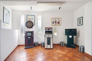 A room with a dartboard, a vending machine, a television, and framed artwork on the walls.