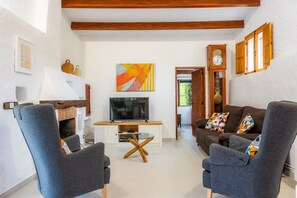 A living room with a TV, two armchairs, a glass coffee table, a fireplace, and a clock on the wall.