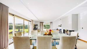 A modern dining area with a glass table, four chairs, and a view of the outdoors.