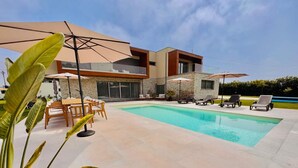 A modern house with a swimming pool, outdoor furniture, and umbrellas.