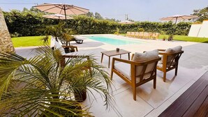A poolside area with outdoor furniture, umbrellas, and a well-maintained lawn.