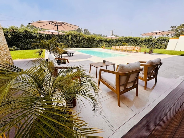 A poolside area with outdoor furniture, umbrellas, and a well-maintained lawn.