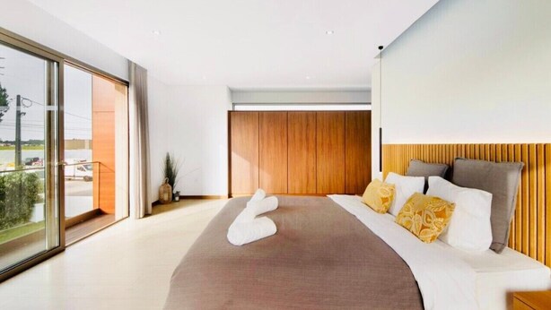A modern bedroom with a large bed, a wooden headboard, and a view through a sliding glass door.