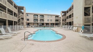 A swimming pool surrounded by lounge chairs and a multi-story building with balconies. - Las Palmas 114- Pool, BBQ, short walk to beach (Gulf Shores)