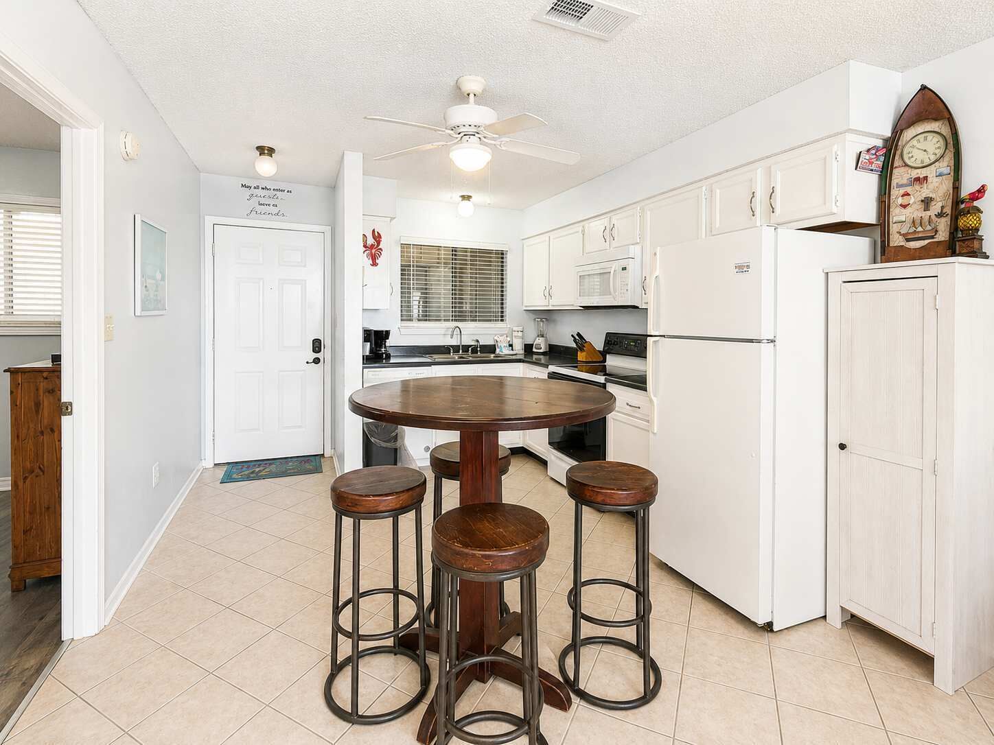 Una cocina con una mesa redonda y cuatro taburetes, muebles blancos, un microondas y un refrigerador.