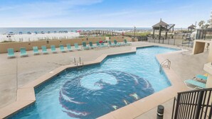 A swimming pool with lounge chairs and a view of the beach.