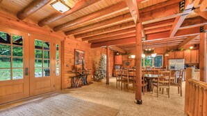 Interior espacioso de una cabaña de troncos con comedor, cocina y ventanas amplias que ofrecen vistas al exterior.