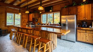 Una cocina rústica con taburetes de madera, una isla grande, electrodomésticos de acero inoxidable y vistas al exterior.