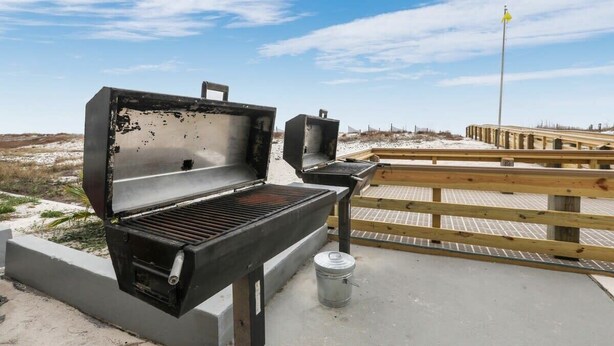 An outdoor grill area with a wooden deck and a clear sky. - Island Wind West 177, Next to Hangout, Beachfront (Gulf Shores)