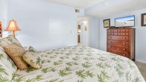A bedroom with a bed, a dresser, a television, and a door leading to another room. - Island Wind West 177, Next to Hangout, Beachfront (Gulf Shores)