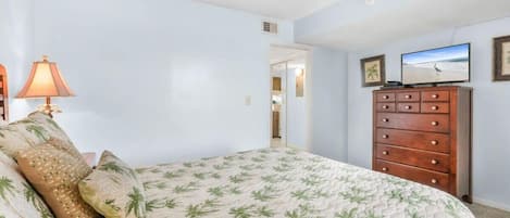 Um quarto com uma cama, cômoda, televisão e porta para outro espaço.