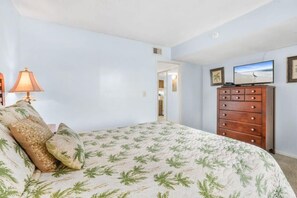 Ein Schlafzimmer mit einem Bett, einem Schminktisch, einem Fernseher und einer Tür zu einem anderen Raum.