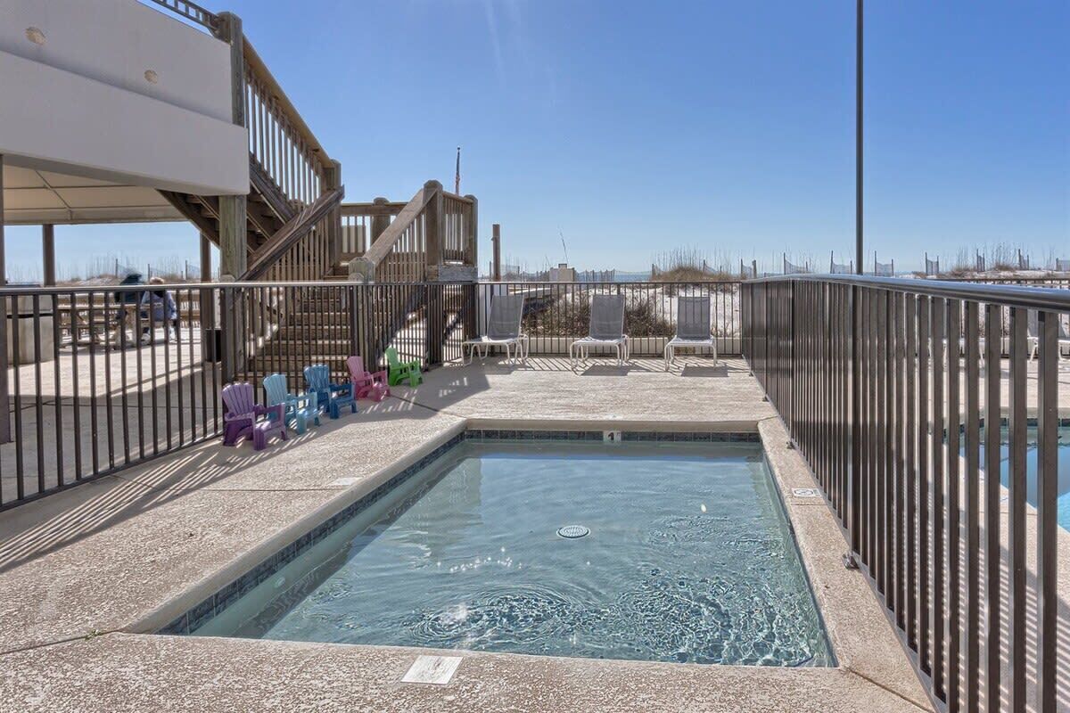 A swimming pool with a wooden deck and chairs, surrounded by a metal fence.