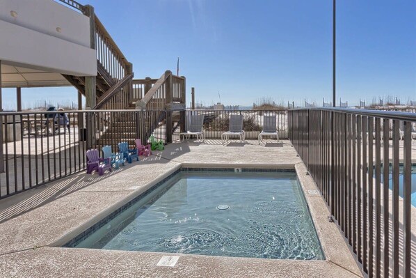 Piscina con cubierta de madera y sillas, rodeada por una cerca de metal.