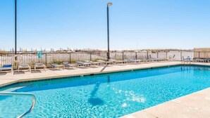 A swimming pool with lounge chairs and a fence, surrounded by a clear sky. - Island Wind West 177, Next to Hangout, Beachfront (Gulf Shores)