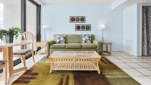 A living room with a sofa, coffee table, and chairs. There are two wall art pieces above the sofa. - Island Wind West 177, Next to Hangout, Beachfront (Gulf Shores)