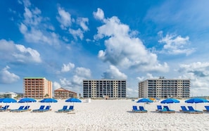 Una playa con tumbonas y sombrillas, un edificio de hotel y un cielo despejado.