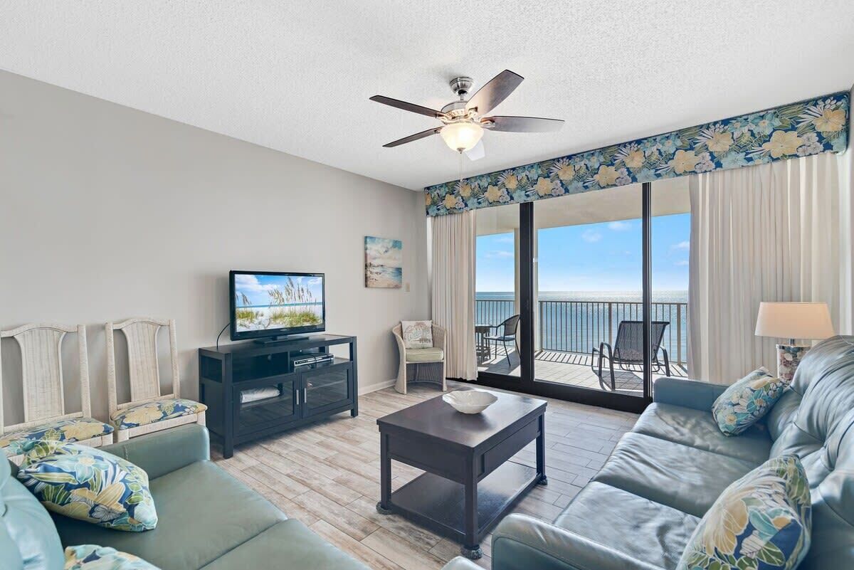 A living room with a television, sofa, coffee table, and a balcony with outdoor furniture.
