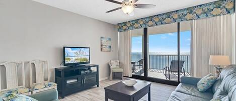 A living room with a television, sofa, coffee table, and a balcony with outdoor furniture.
