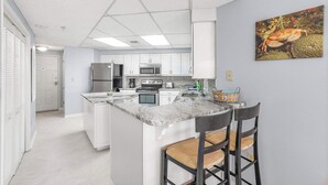A modern kitchen with white cabinets, a marble countertop, and a central island with two bar stools.