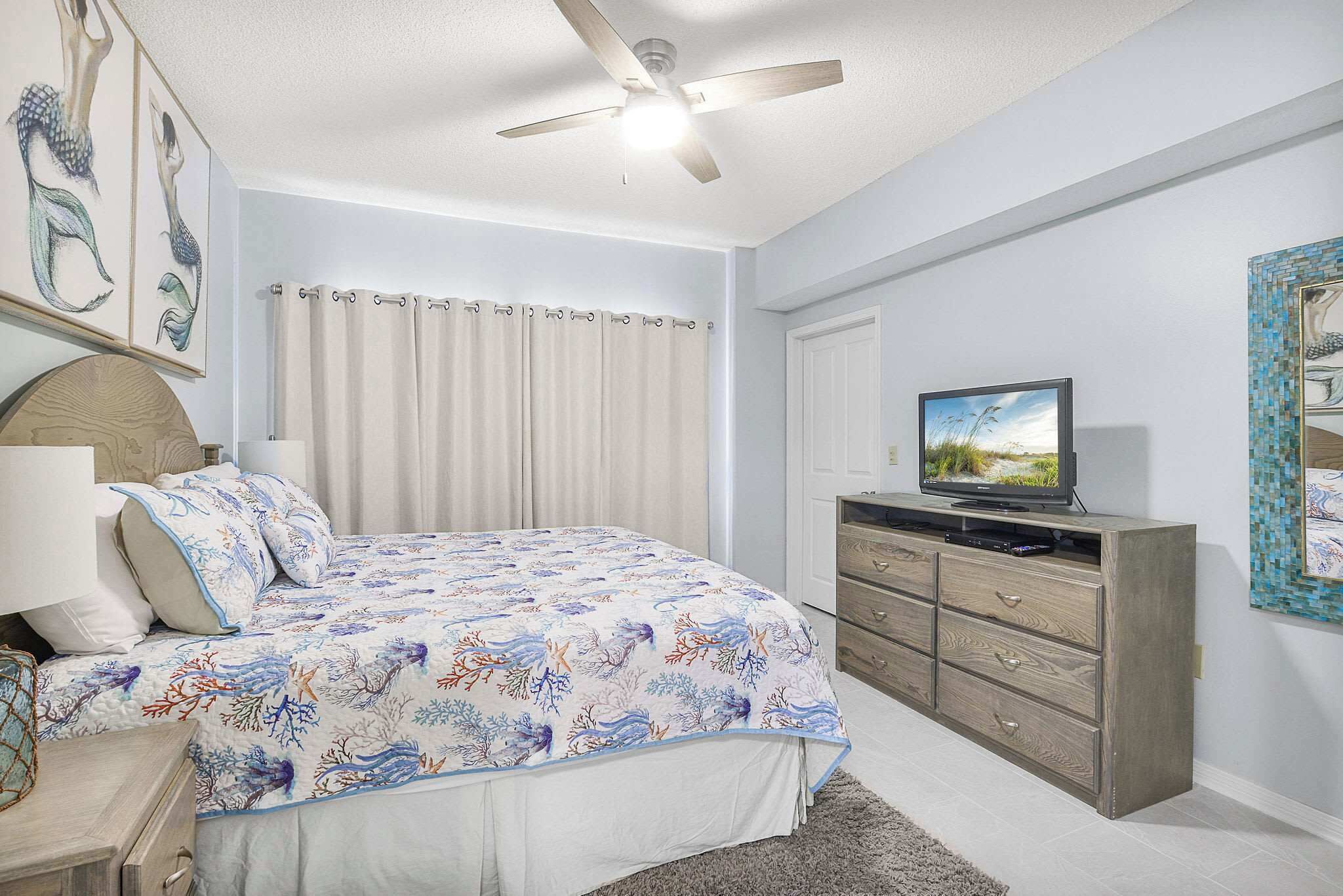A bedroom with a bed, a TV, a ceiling fan, and a dresser.