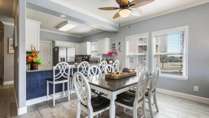 A modern kitchen with white cabinets, a dining area with white chairs, and a ceiling fan.