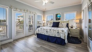 A bedroom with a bed, a ceiling fan, a nightstand, and a window with a view of a building.