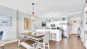 A modern kitchen with white cabinetry, a central island, and a dining area with a wooden table and white chairs.