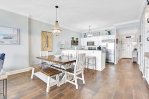 A modern kitchen with white cabinetry, a central island, and a dining area with a wooden table and white chairs.