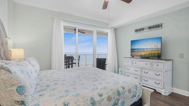 A bedroom with a bed, a dresser, a television, and a balcony with a view. - Regency Isle 806 | Gulffront Condo w/Stunning Views, Pools & Sauna (Orange Beach)