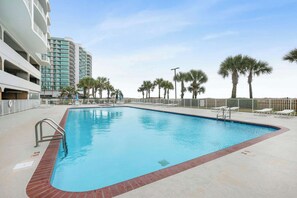 A swimming pool with a red brick border, surrounded by palm trees and a white fence.