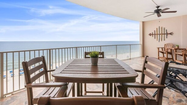 A balcony with a table and chairs, a ceiling fan, and a view of the beach.