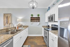 A kitchen with white cabinets, granite countertops, stainless steel appliances, and a hanging light fixture.