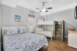 A bedroom with a bed, a bunk bed, a ceiling fan, a window with blinds, and a wall-mounted TV.
