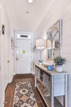 A hallway with a white door, a blue sign reading "GO BOATING", a lamp, a mirror, and a patterned rug.