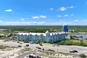 A large hotel with a distinctive blue facade and a prominent cylindrical tower, situated by a road with moderate traffic and a body of water in the background.