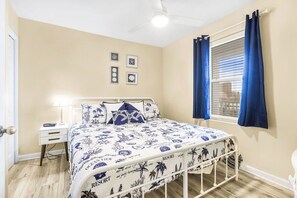 Un dormitorio con cama, mesita de noche, ventana con cortinas y adornos en la pared.