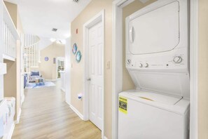 A laundry room with a front-loading washer and dryer, a spiral staircase, and a living area in the background.
