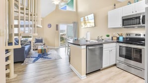 Une cuisine moderne dotée d’un îlot central, d’appareils électroménagers en acier inoxydable et d’un coin repas agrémenté d’un tapis bleu.