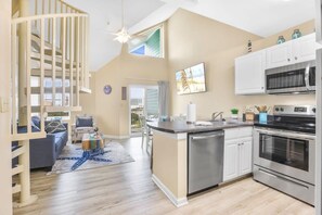 A modern kitchen with a central island, stainless steel appliances, and a dining area with a blue rug.