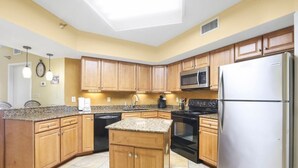 A kitchen with wooden cabinets, granite countertops, a stainless steel refrigerator, and a black stove. - Windward Pointe 305: 3rd floor, Beachfront, pool (Orange Beach)