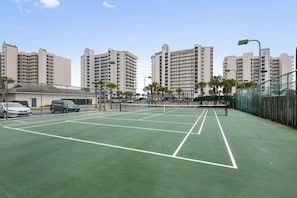 An outdoor tennis court with a net, surrounded by a fence, and adjacent to a parking area with cars. - Windward Pointe 305: 3rd floor, Beachfront, pool (Orange Beach)
