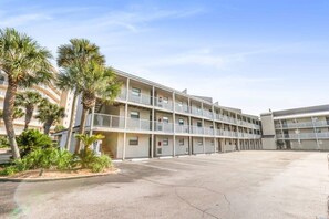 A multi-story motel with balconies, a parking lot, and palm trees.