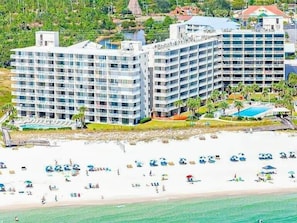 A beachfront hotel with multiple floors, a pool, and beach umbrellas.