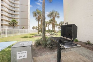A barbecue grill and a sign that reads "HOT COALS ONLY!" in a courtyard with palm trees and a building in the background.
