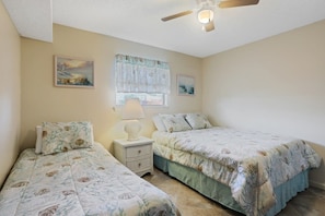 A bedroom with two beds, a ceiling fan, a nightstand with a lamp, and artwork on the walls.