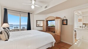 A hotel room with a bed, a TV, a wooden cabinet, and a balcony with a view of the sea.