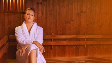 A person sitting in a wooden sauna with benches and a wooden wall.